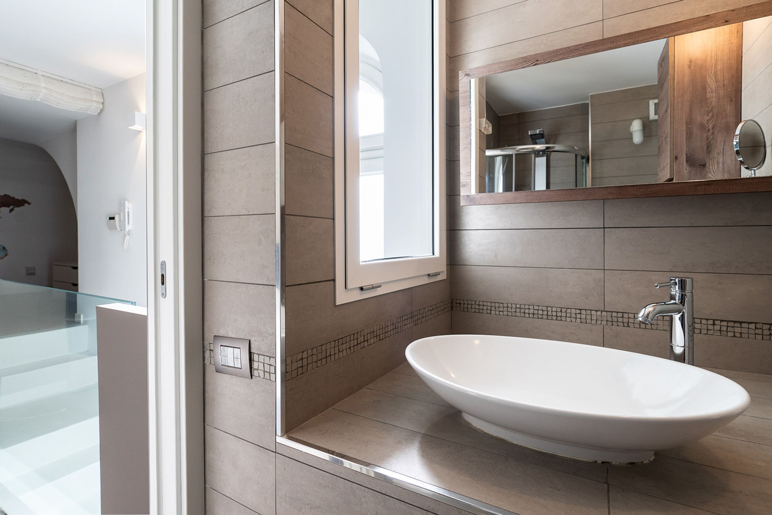A modern bathroom with a large oval sink, a mirror, and a shower area.