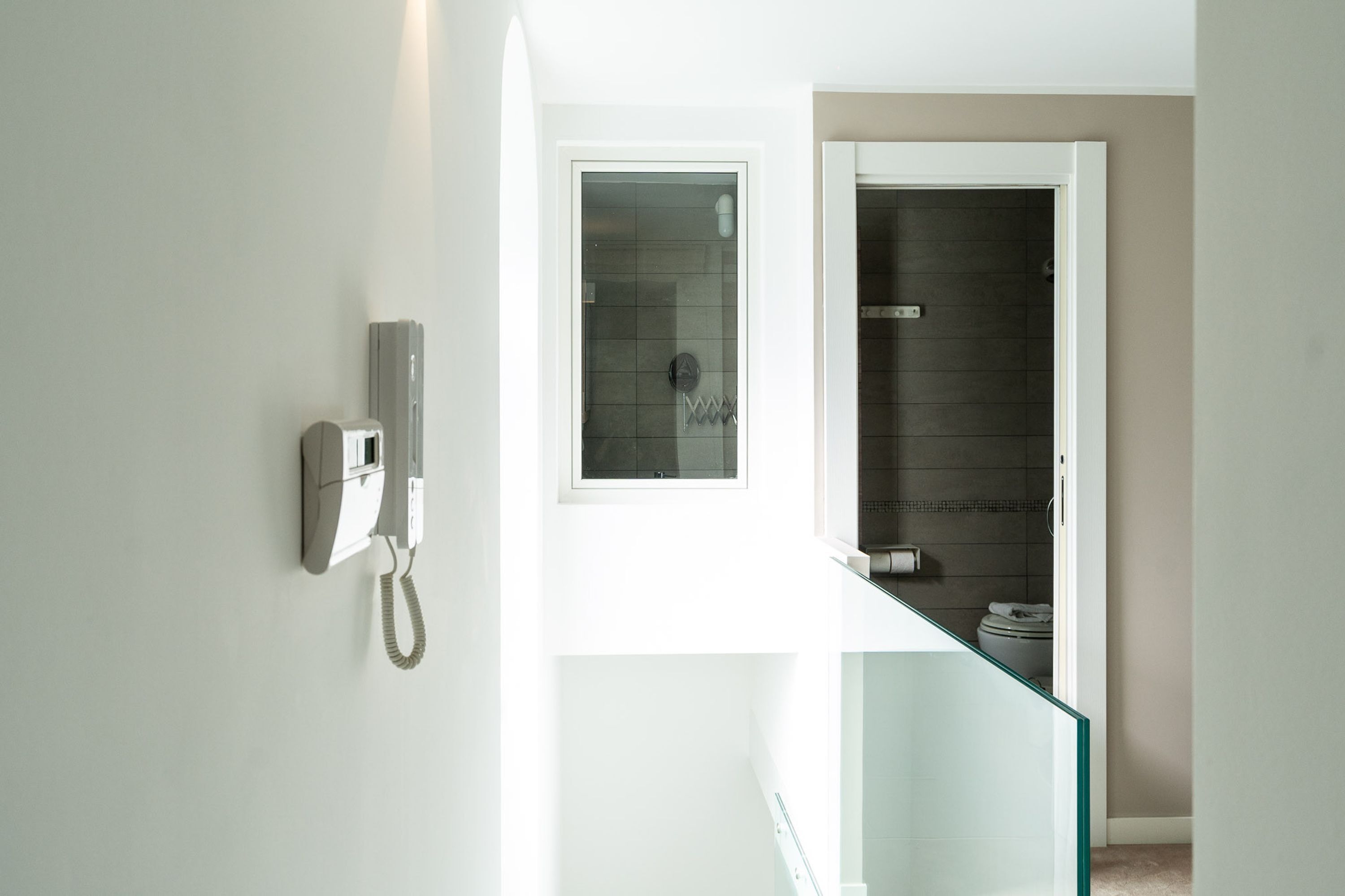 Une salle de bain moderne avec une douche à parois de verre, un téléphone fixé au mur et des toilettes apparentes.