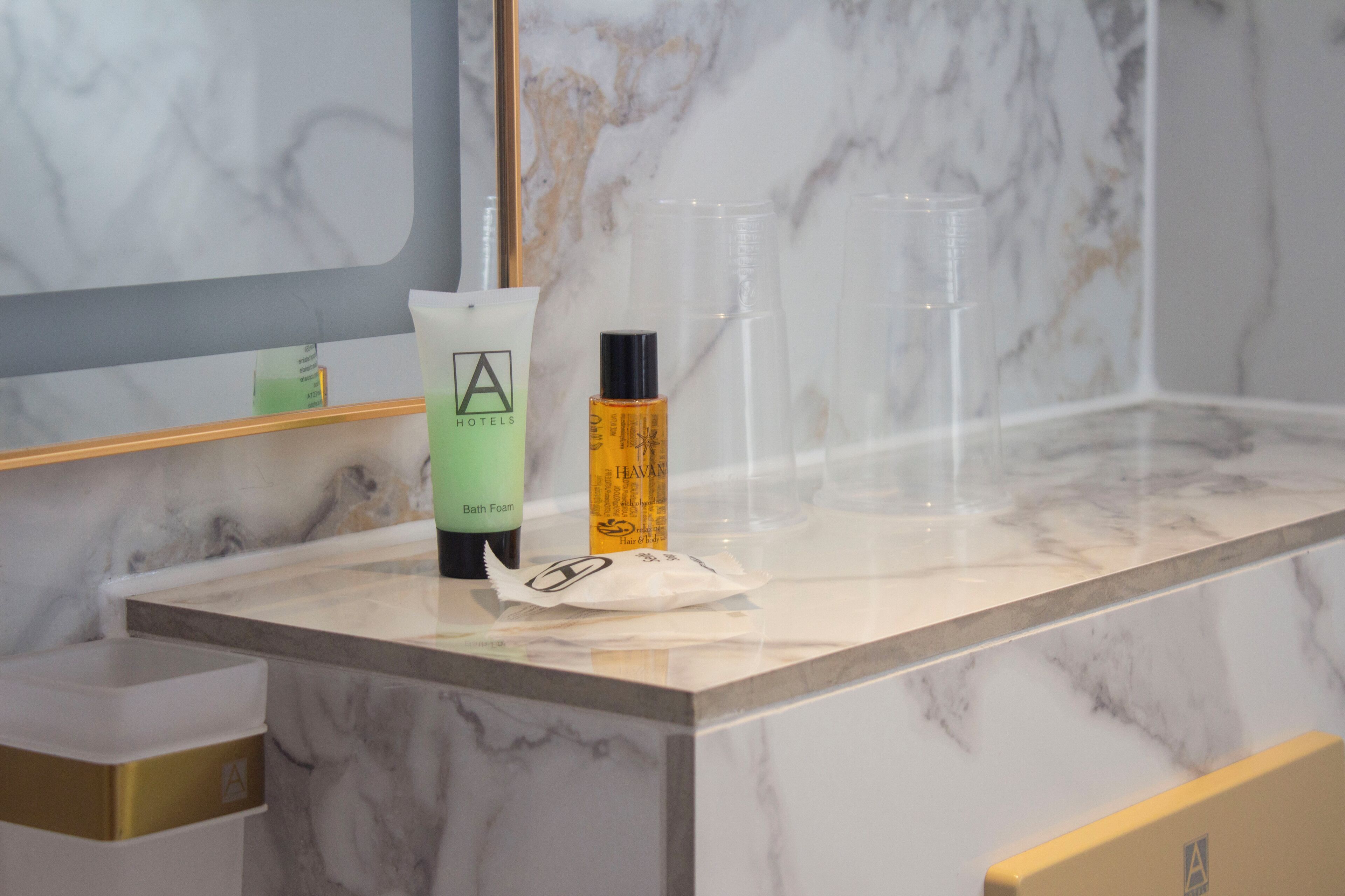 A bathroom counter with a bottle of bath foam, a bottle of lotion, and a clear plastic cup.