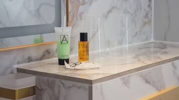 A bathroom counter with a bottle of bath foam, a bottle of lotion, and a clear plastic cup.