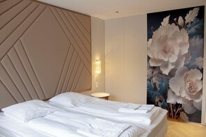 A bedroom with a bed, a wall-mounted light, and a floral painting.