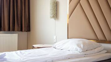 Una cama bien tendida con sábanas blancas, un cabecero con diseño geométrico y una lámpara de pared.
