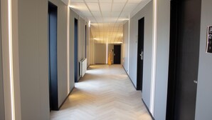 Un pasillo moderno de hotel con piso de madera clara, paredes blancas y puertas oscuras.