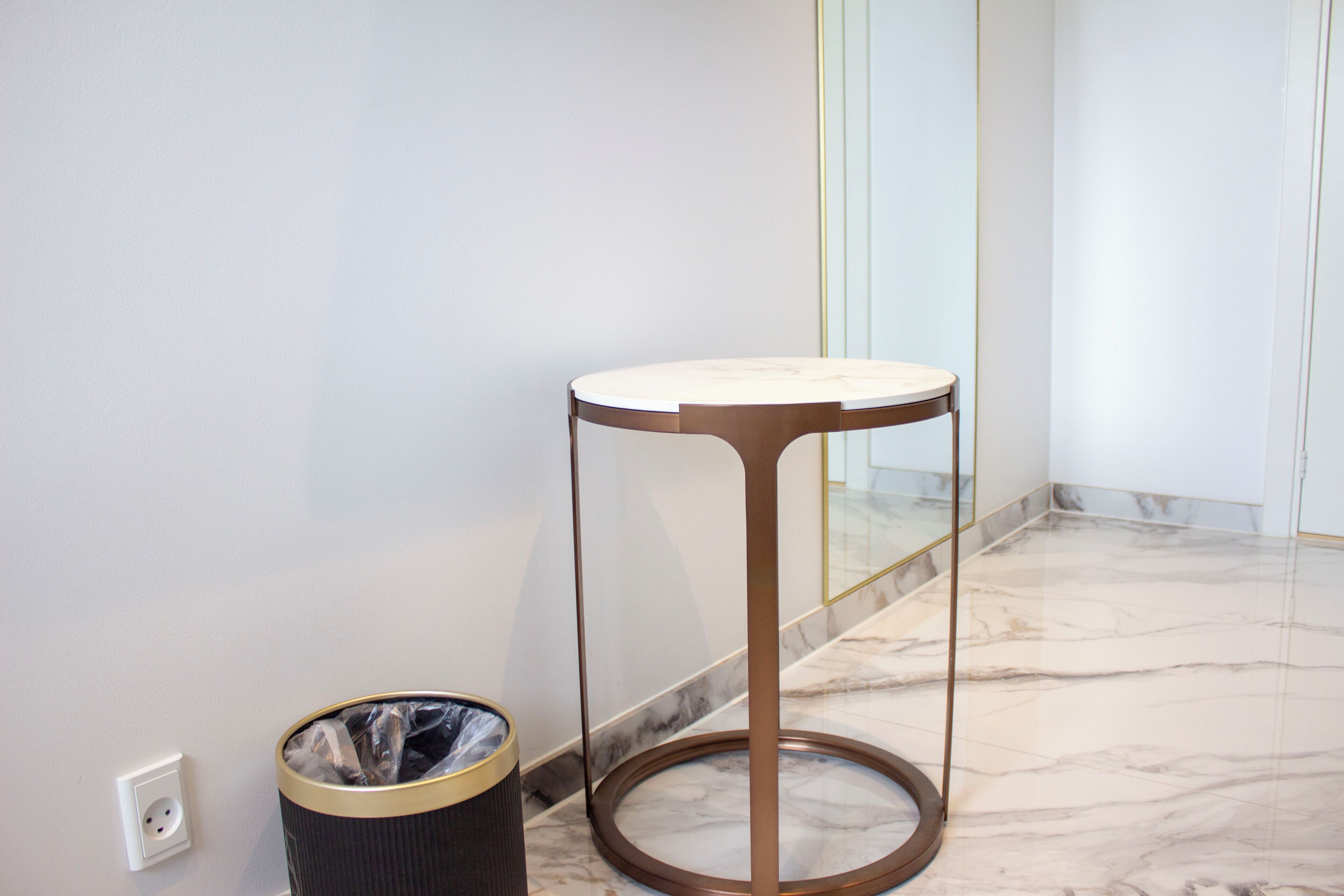 A corner of a room with a marble floor, a round table with a metal base, and a trash can.
