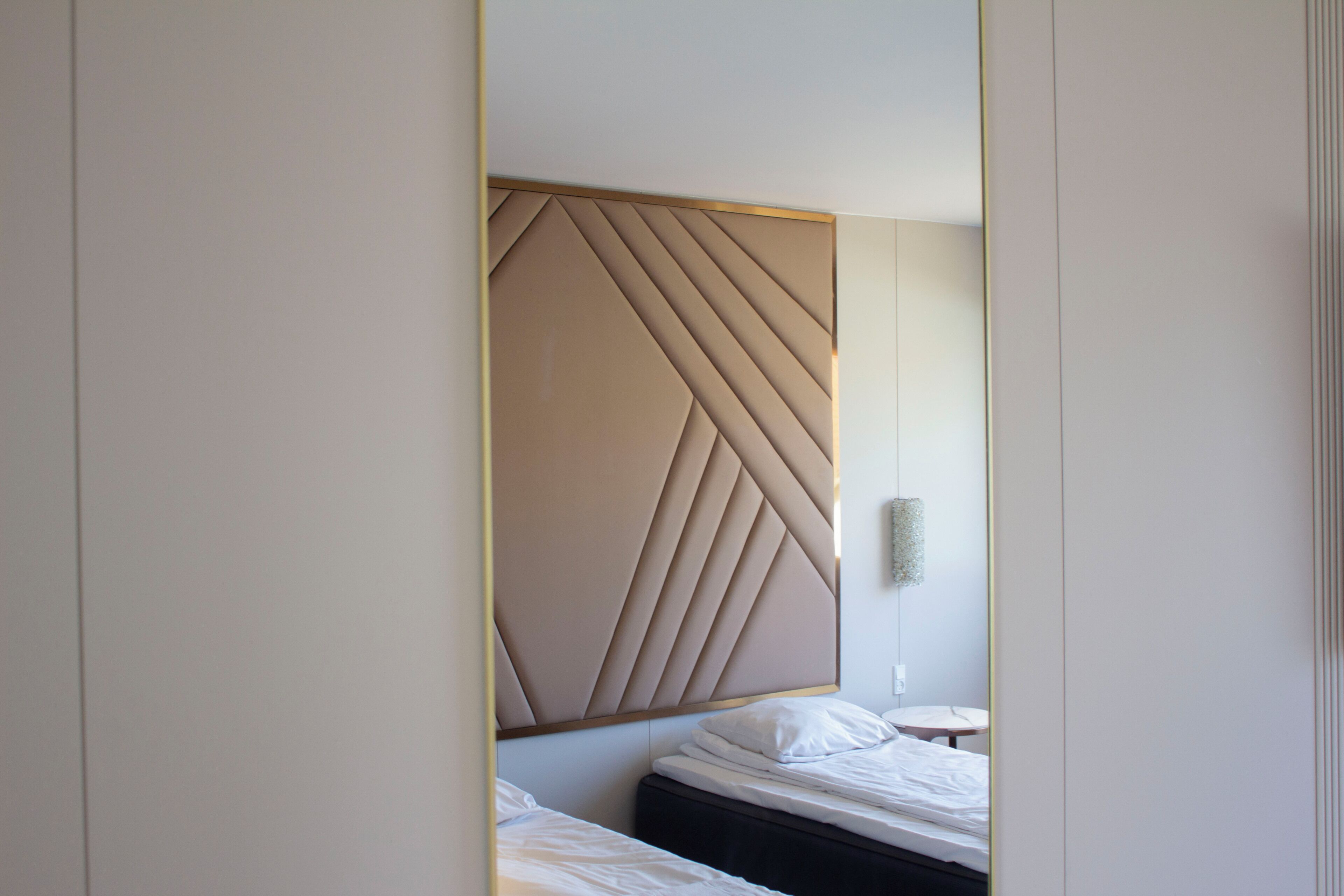 Una camera d'albergo moderna con una testiera geometrica, un comodino e un punto luce a parete.