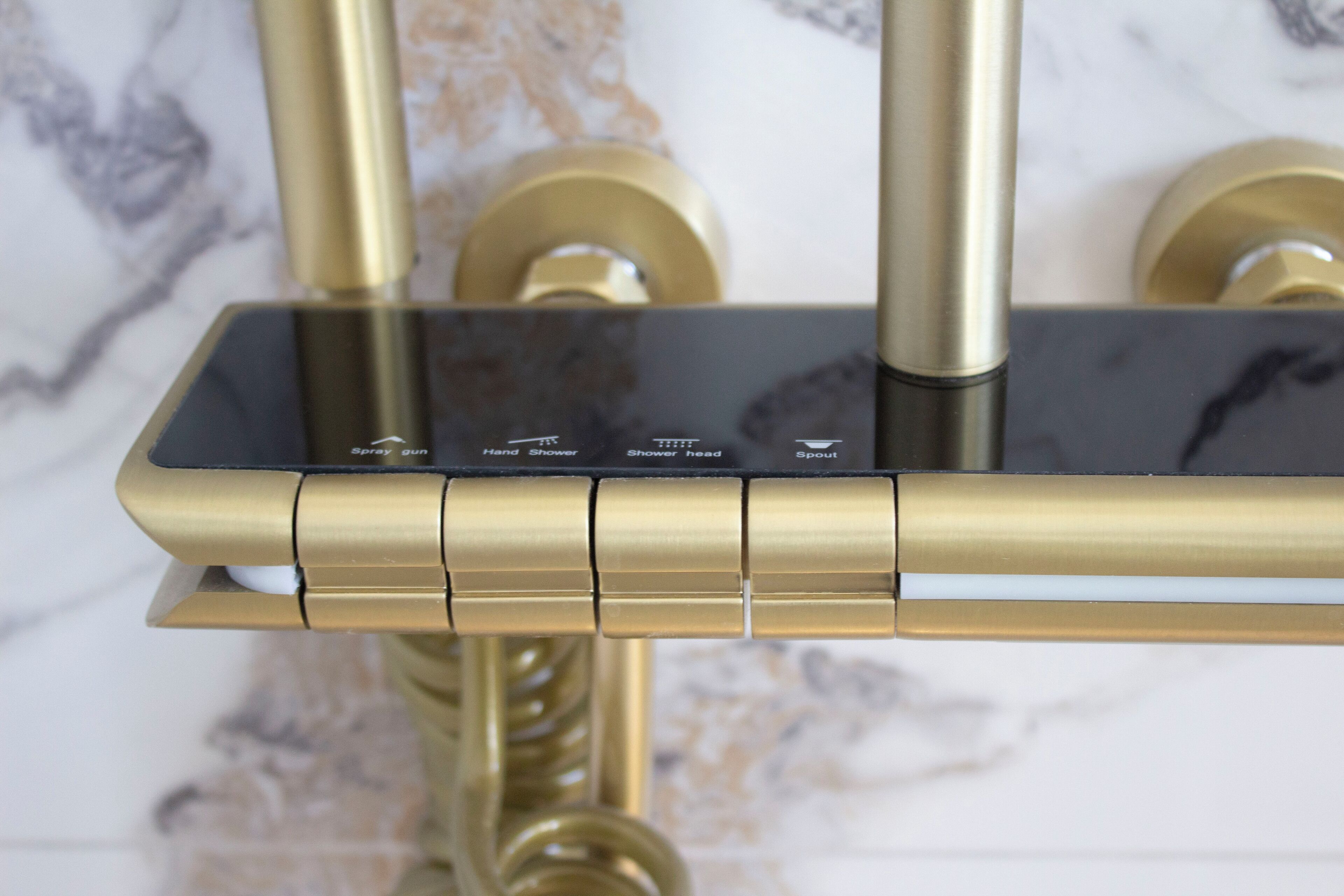 A modern bathroom with a gold faucet, a black control panel, and a marble backsplash.