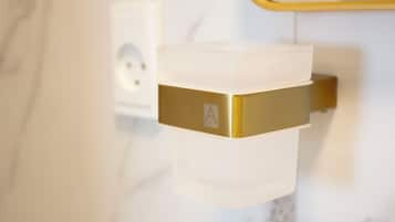 A bathroom with a white marble wall, a gold-colored towel warmer, and a white towel dispenser.