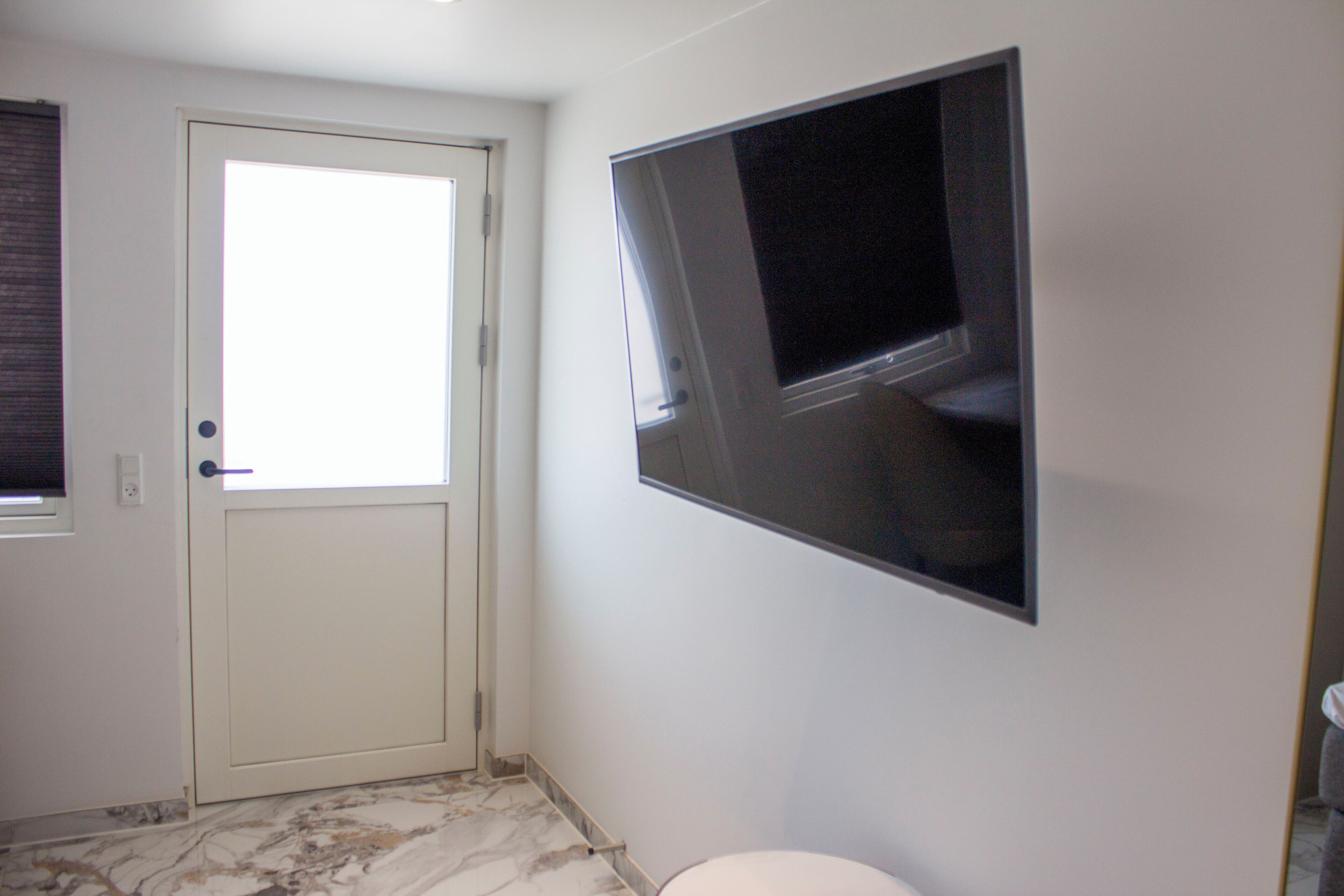 A bathroom with a toilet, a door, and a wall-mounted TV.