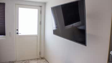 A bathroom with a toilet, a door, and a wall-mounted TV.