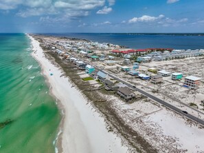 Vista aérea de uma área costeira com praia, estrada e edifícios com diferentes cores de telhado.