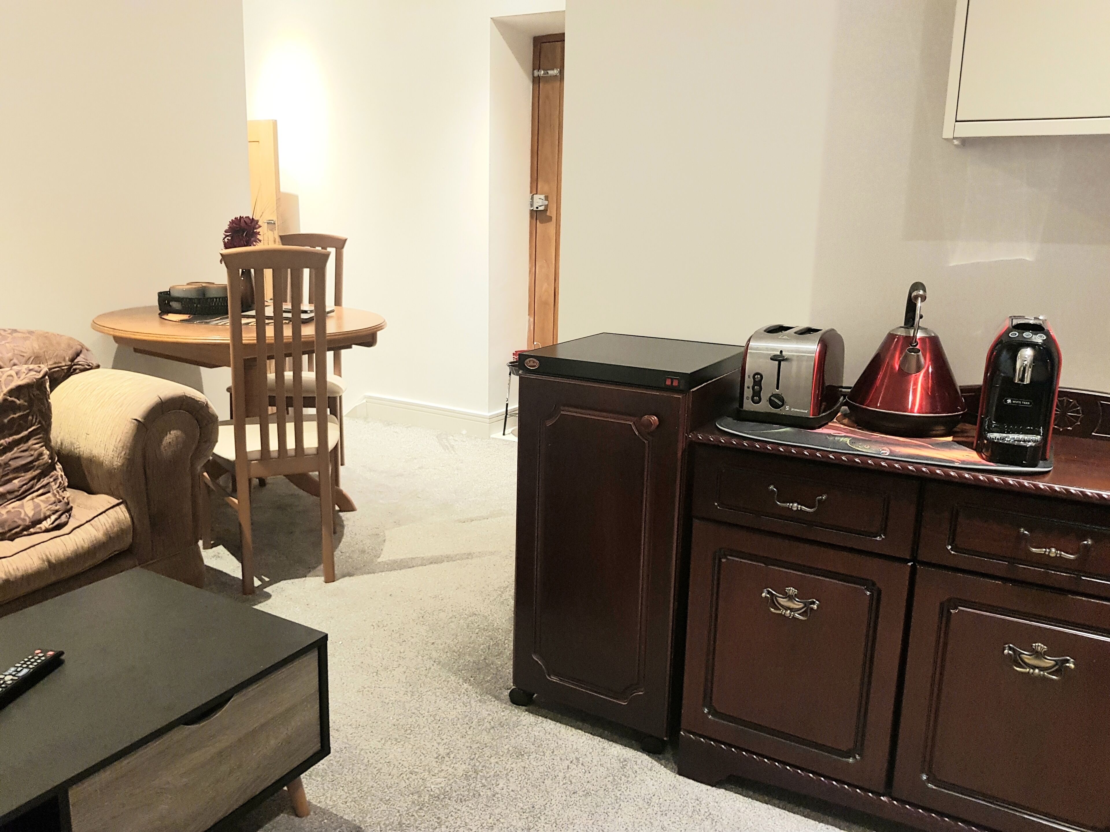 A compact living space with a wooden dining table, a sofa, a cabinet with drawers, and a coffee maker on the counter.