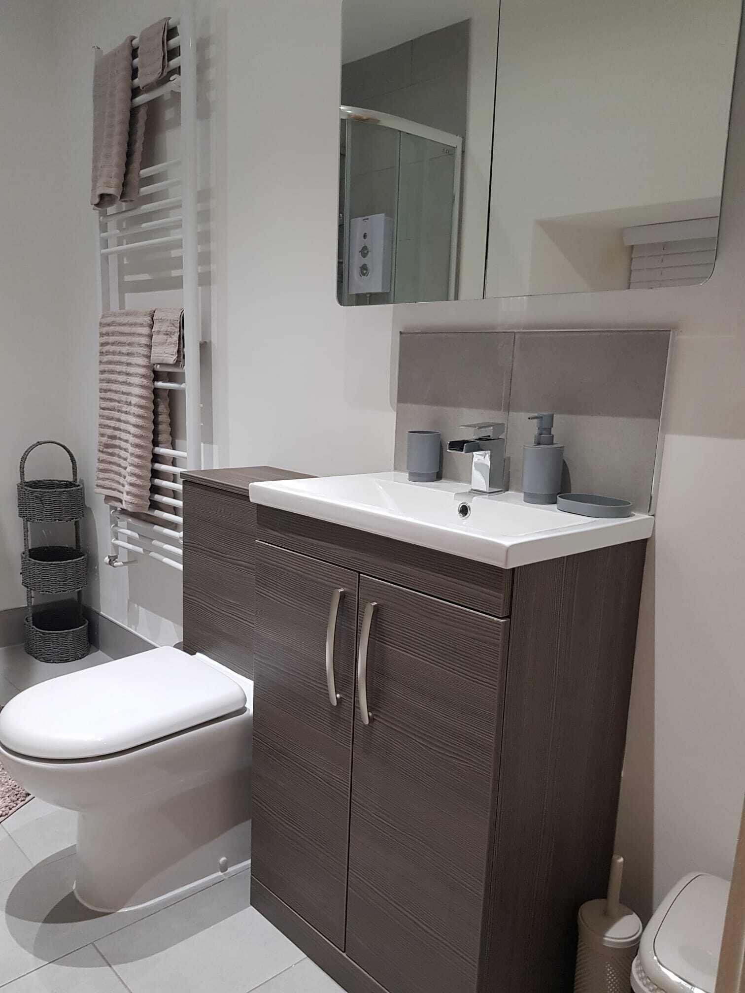 Een moderne badkamer met toilet, een wastafel met spiegel en een handdoekrek.