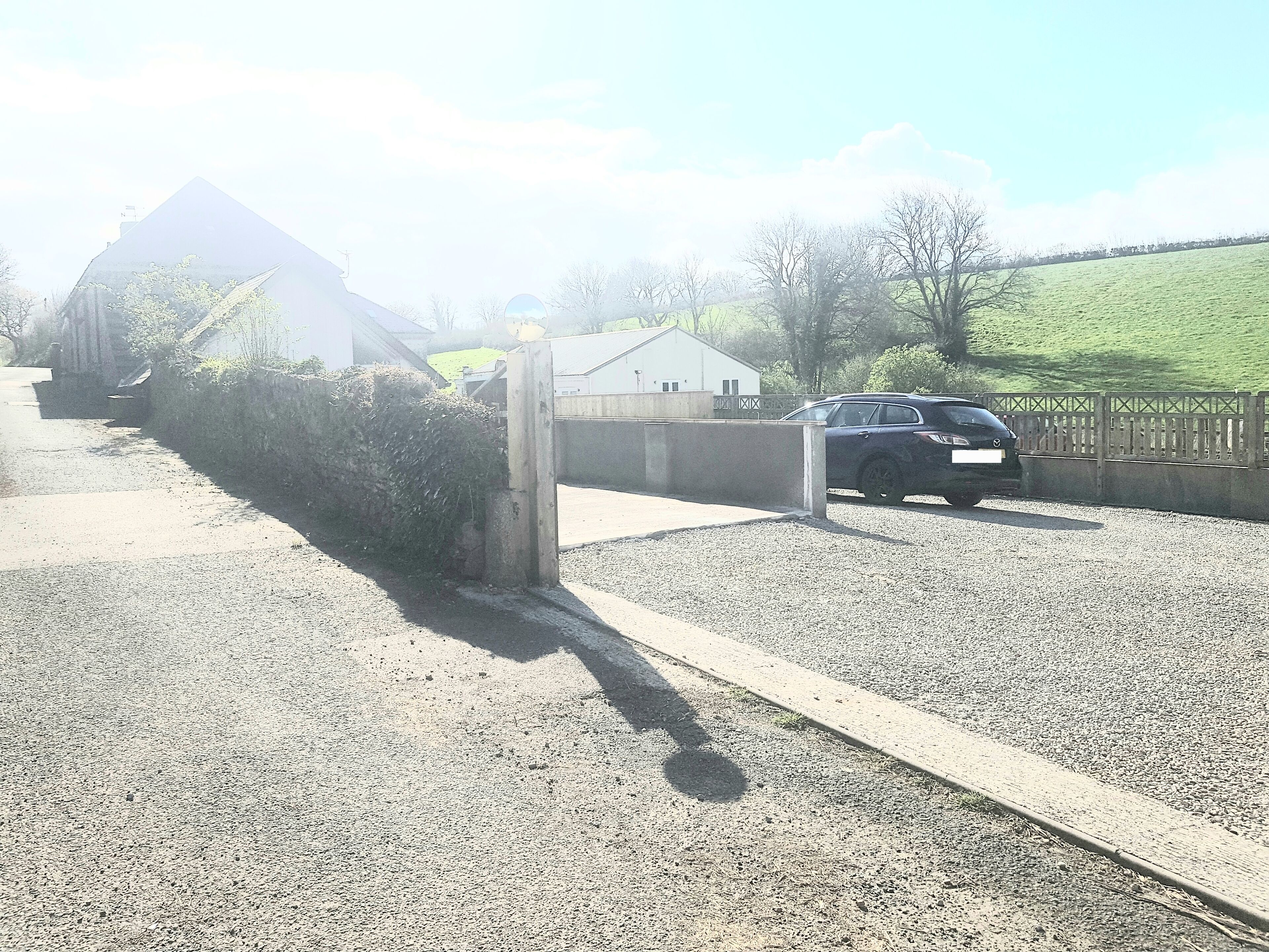 A gravel driveway leading to a gated entrance with a car parked inside.