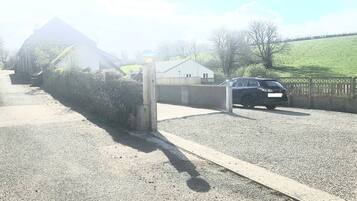 A gravel driveway leading to a gated entrance with a car parked inside.