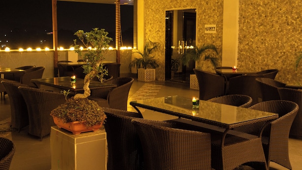 An outdoor seating area with wicker furniture, potted plants, and a glass table. - Trevon The Shire Inn (Haldwani)