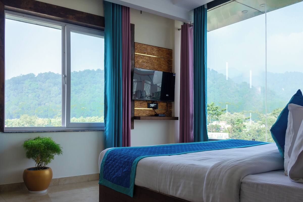A bedroom with a large bed, a TV mounted on the wall, and a view of a forested area.