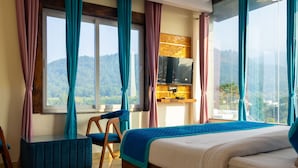 A hotel room with a large bed, a small table, a chair, and a view of the mountains. - Trevon The Shire Inn (Haldwani)