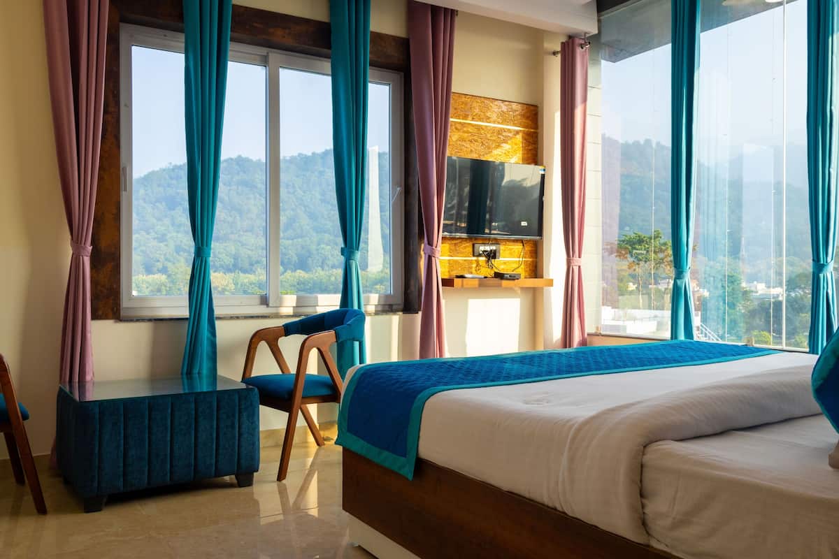 A hotel room with a large bed, a small table, a chair, and a view of the mountains.