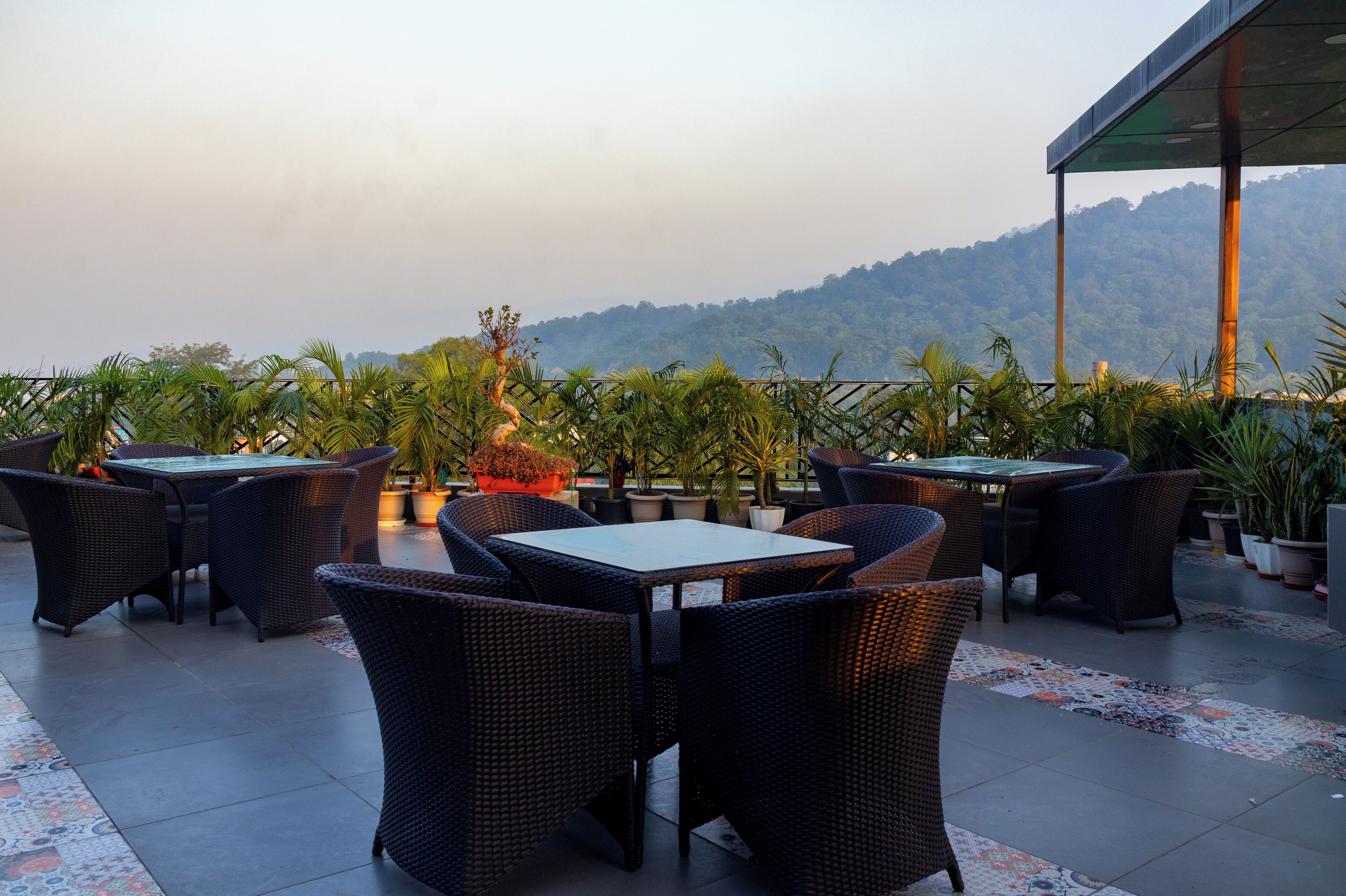An outdoor patio with wicker furniture and potted plants, overlooking a mountainous landscape.
