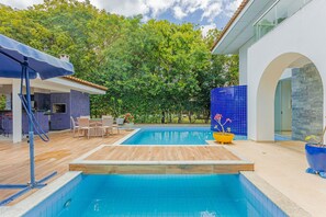 A swimming pool with a wooden deck, surrounded by outdoor furniture and potted plants. - SA08 Casa 5 Suítes - Quintas do Sauípe (Mata de São João)