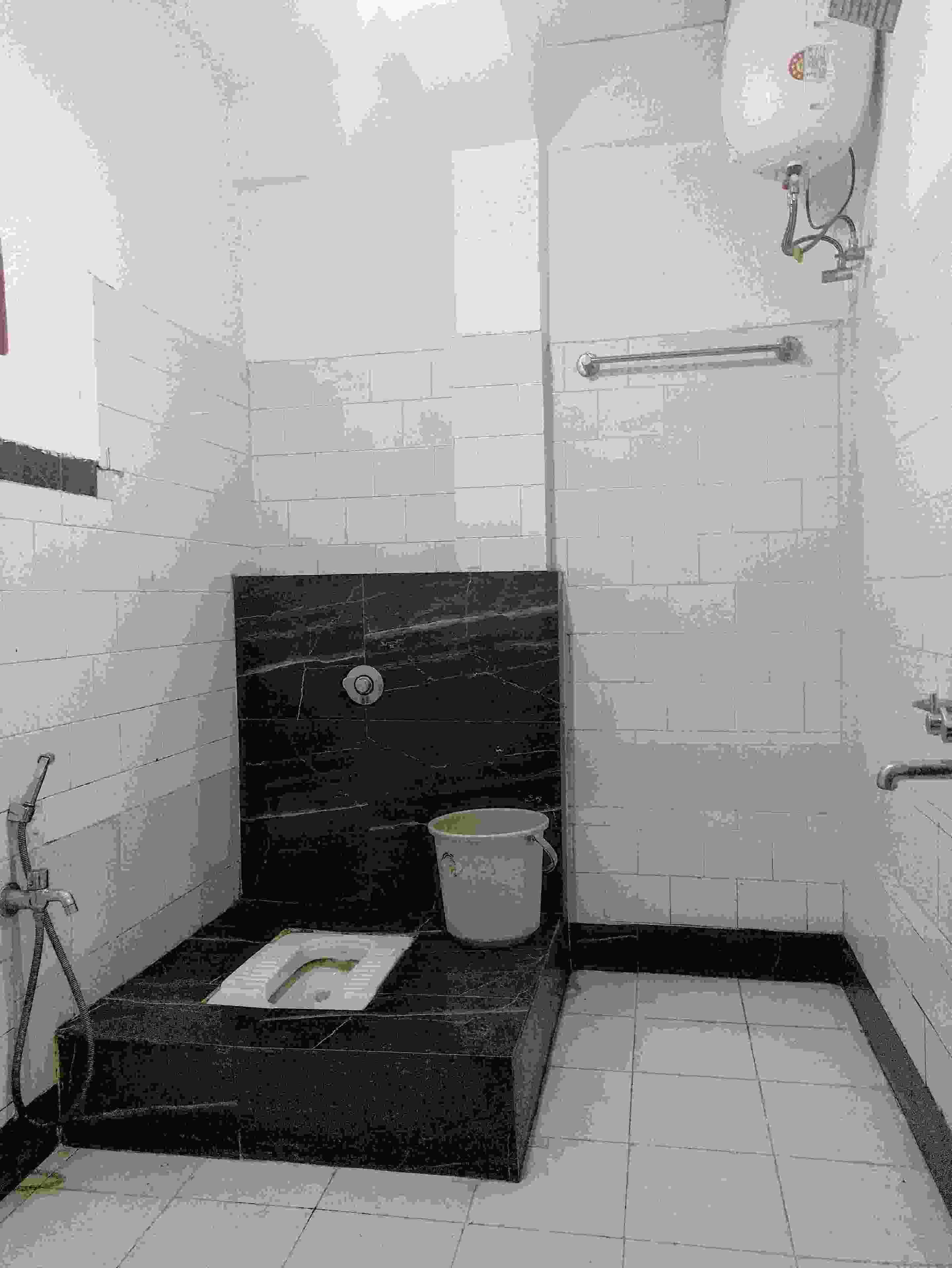 A small, tiled bathroom with a black marble sink, a white bucket, and a towel rack.
