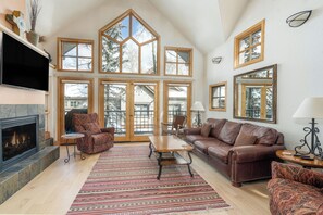 A spacious living room with a fireplace, large windows, and a high ceiling. - Mountain View Haven - 2 Bedroom Luxury Condo Steps from Ski Resort (Mountain Village)