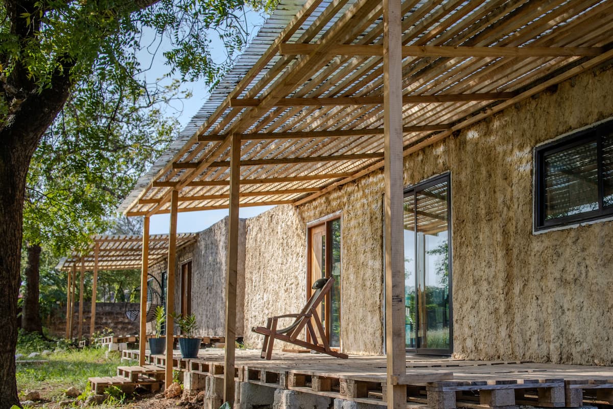 Una pérgola de madera con cubierta de terraza, una mecedora y una planta en maceta.