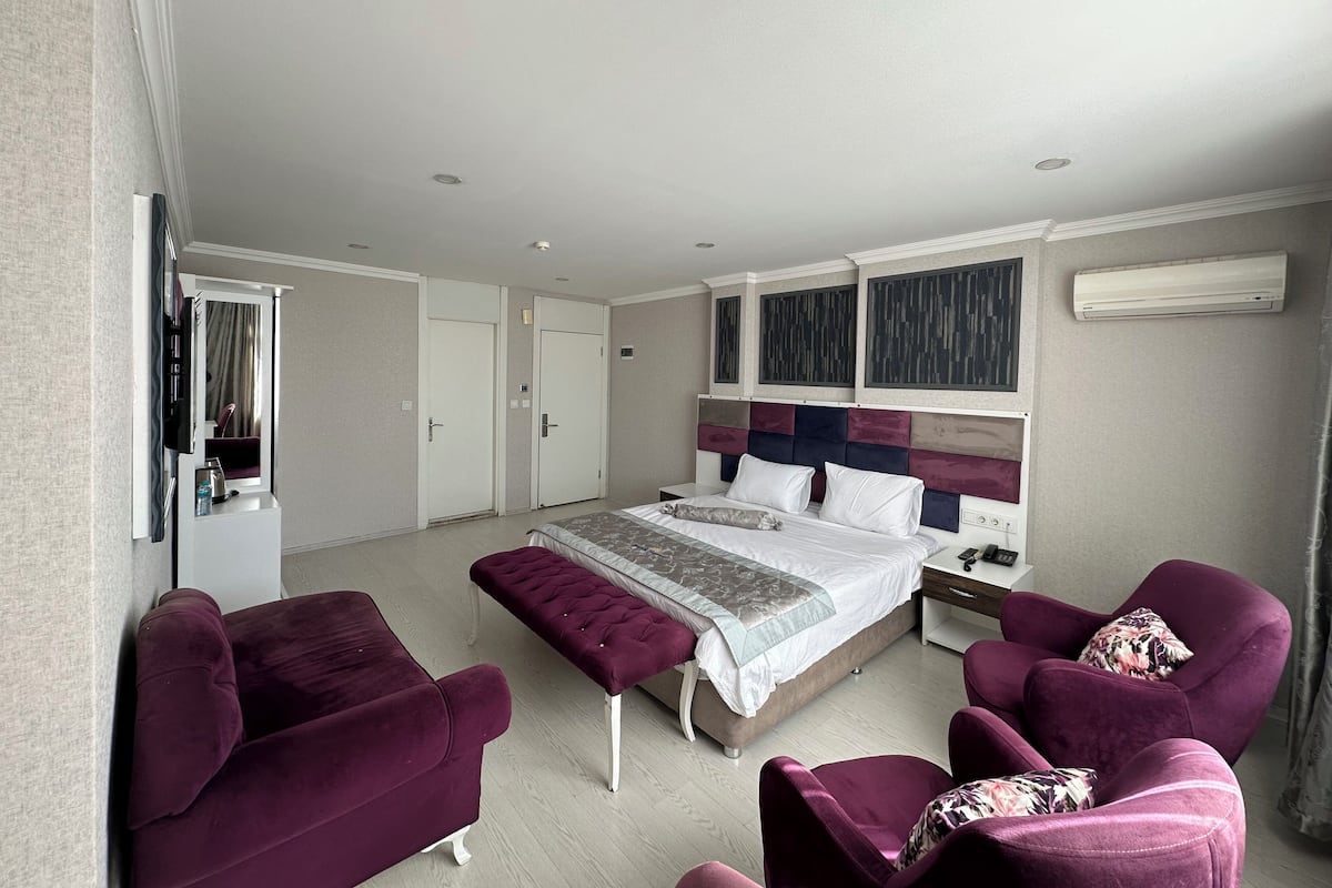 Un dormitorio moderno con una cama grande, dos mesitas de noche, un armario empotrado, una zona de estar con dos sillones y un ventanal con cortinas.