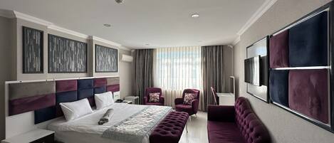 A modern hotel room with a large bed, a sofa, a chair, and a TV.