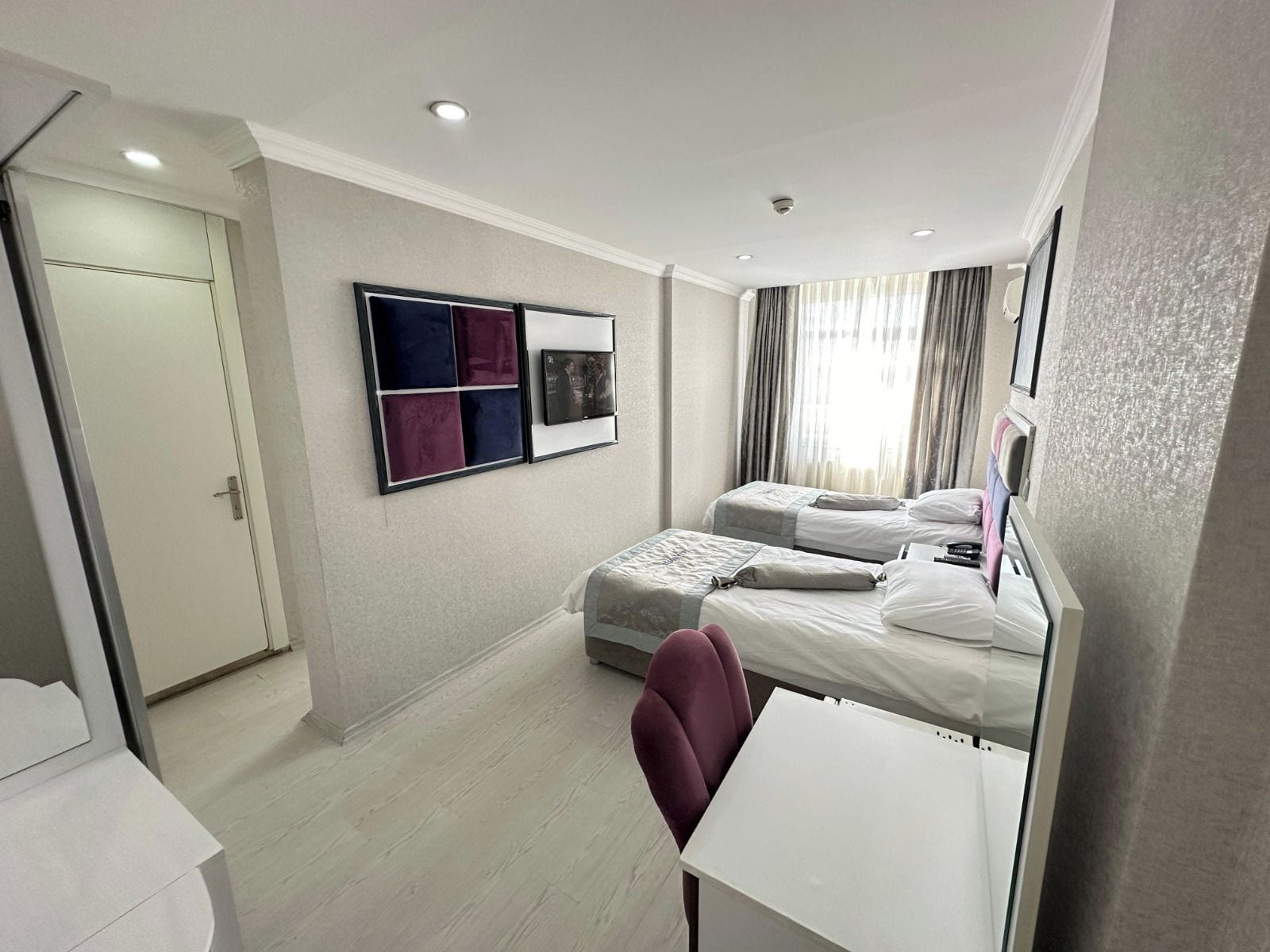 Habitación de hotel con dos camas, un escritorio, una silla, un armario y estante con adornos.