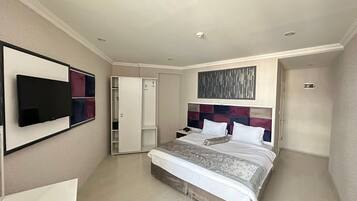 A modern hotel room with a large bed, a wardrobe, a flat-screen TV, and a ceiling-mounted light fixture.