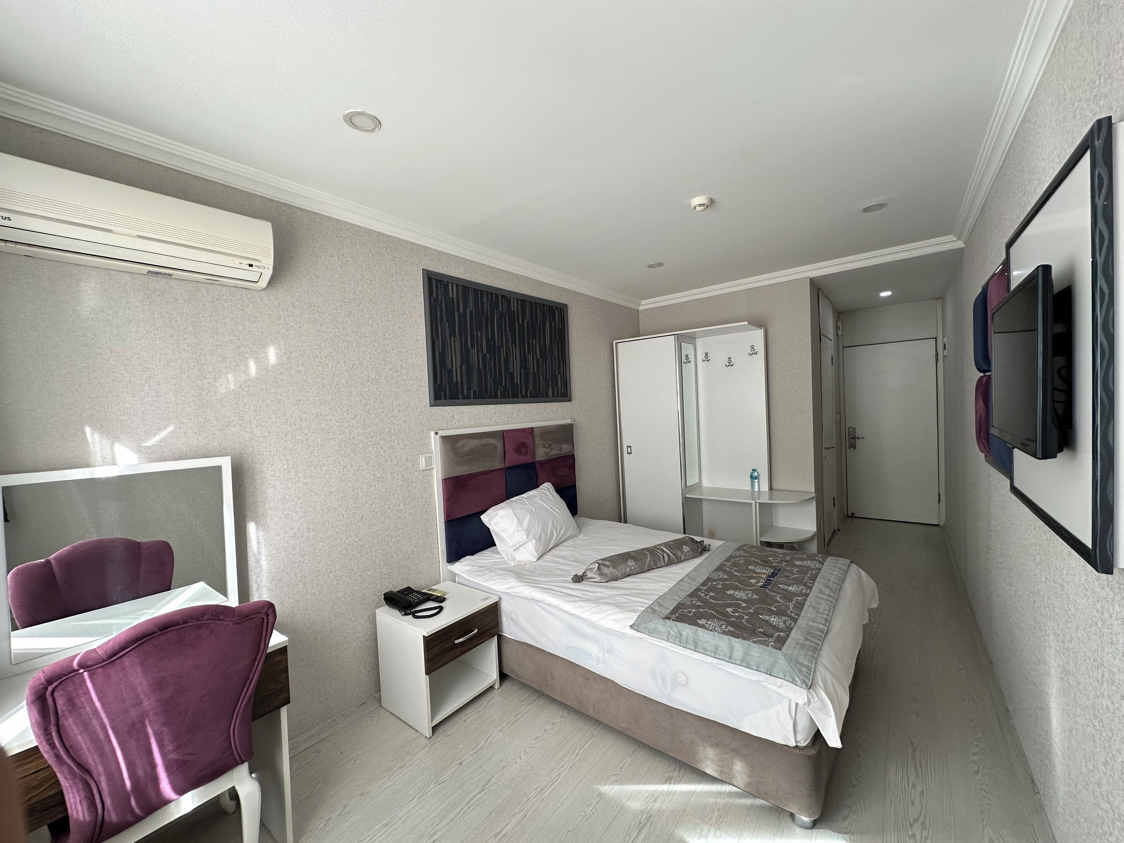 A hotel room with a bed, bedside table, chair, wardrobe, and a TV mounted on the wall.