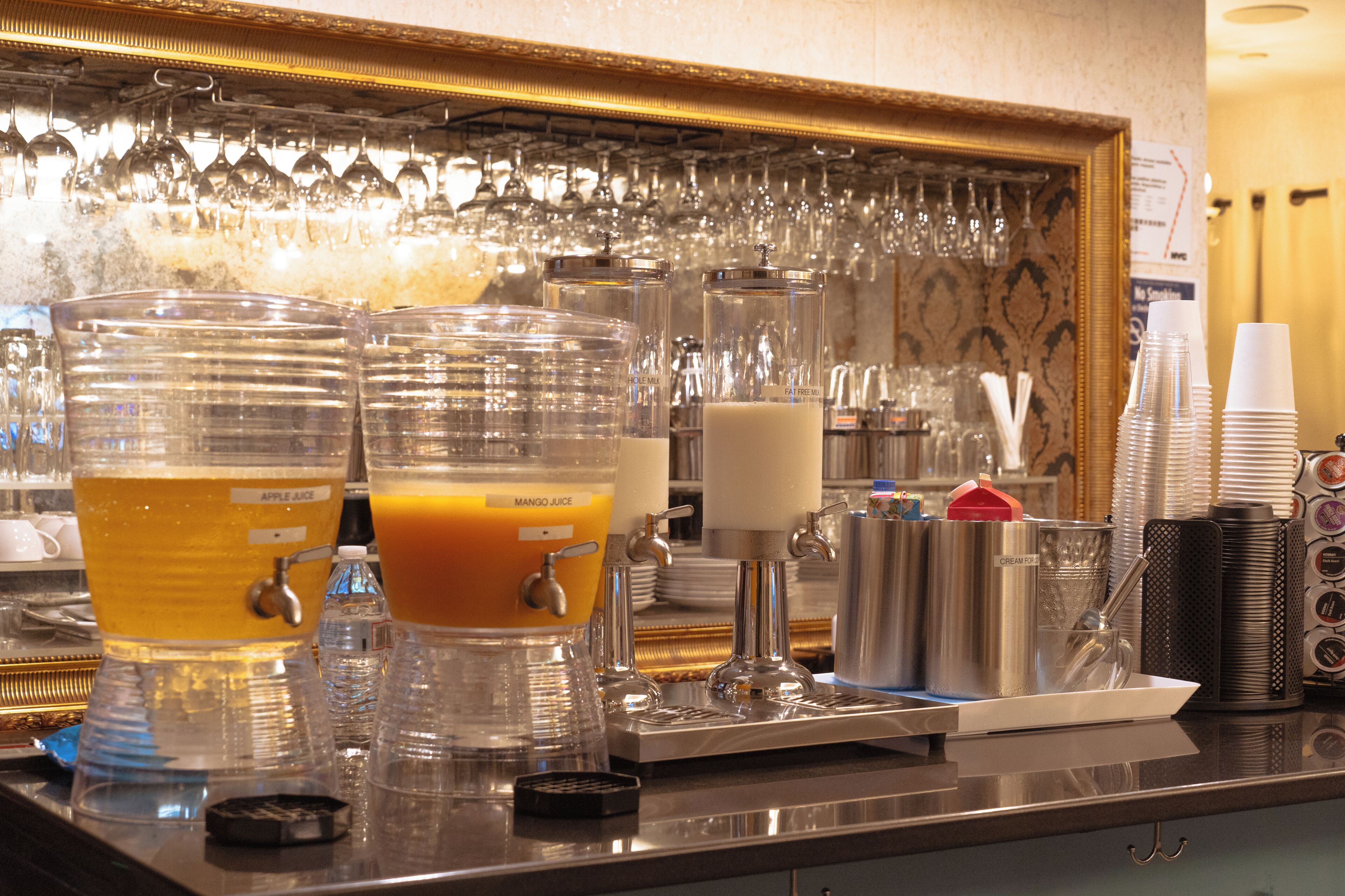 A bar area with multiple beverage dispensers, including apple juice and mango juice, and a variety of glassware.