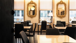 A dining area with tables and chairs, large mirrors on the walls, and a window with a view. - Hotel Stanford (New York)