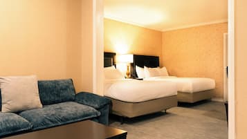 A hotel room with a sofa, two beds, a nightstand, and a lamp.