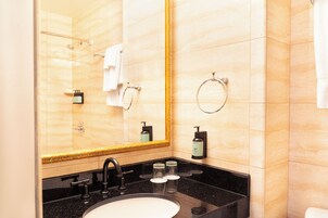 Un baño con un espejo grande, un lavamanos, una ducha y artículos de aseo.