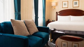 A hotel room with a bed, a sofa, a small round table, and a nightstand. - Hotel Stanford (New York)
