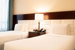A hotel room with two beds, a nightstand with a lamp, a phone, and a digital clock. - Hotel Stanford (New York)
