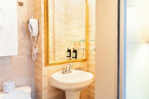 Une salle de bain avec un lavabo blanc, un miroir avec un cadre doré, un distributeur de serviettes et des articles de toilette rangés sur une étagère.