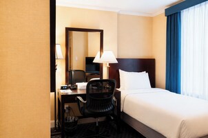 Een hotelkamer met een bed, bureau, stoel en een grote spiegel.