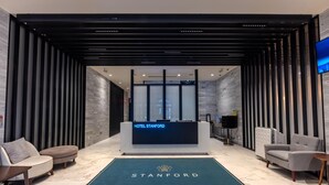 A modern hotel lobby with a reception desk, seating area, and a large screen displaying the hotel name. - Hotel Stanford (New York)
