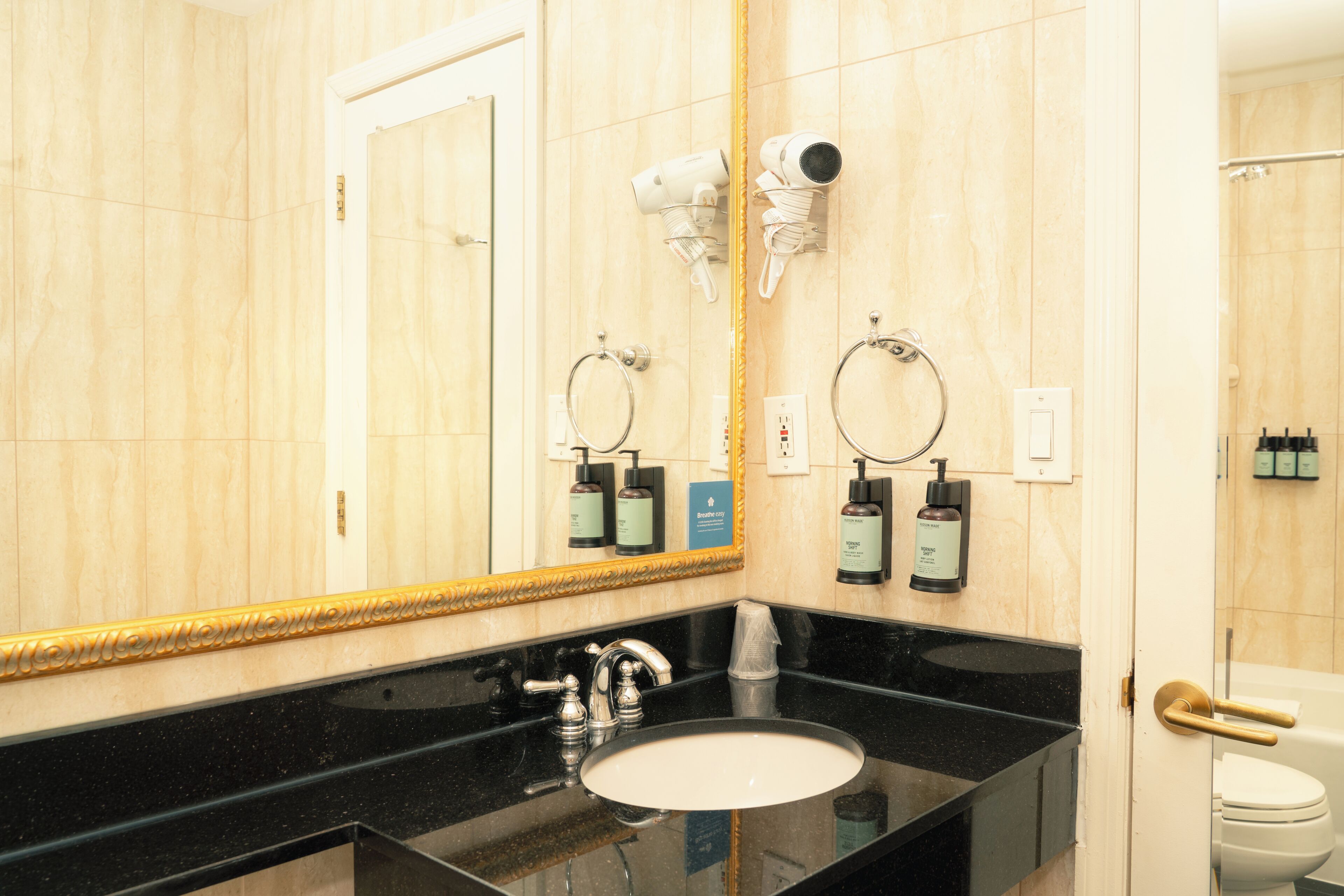 A bathroom with a black sink, a gold-framed mirror, and a toilet.