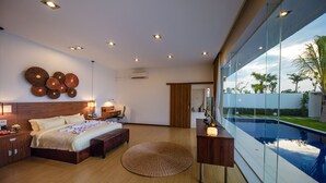 A modern bedroom with a large bed, bedside tables, a round rug, and a view of a swimming pool. - Angkor Rendezvous (Siem Reap)