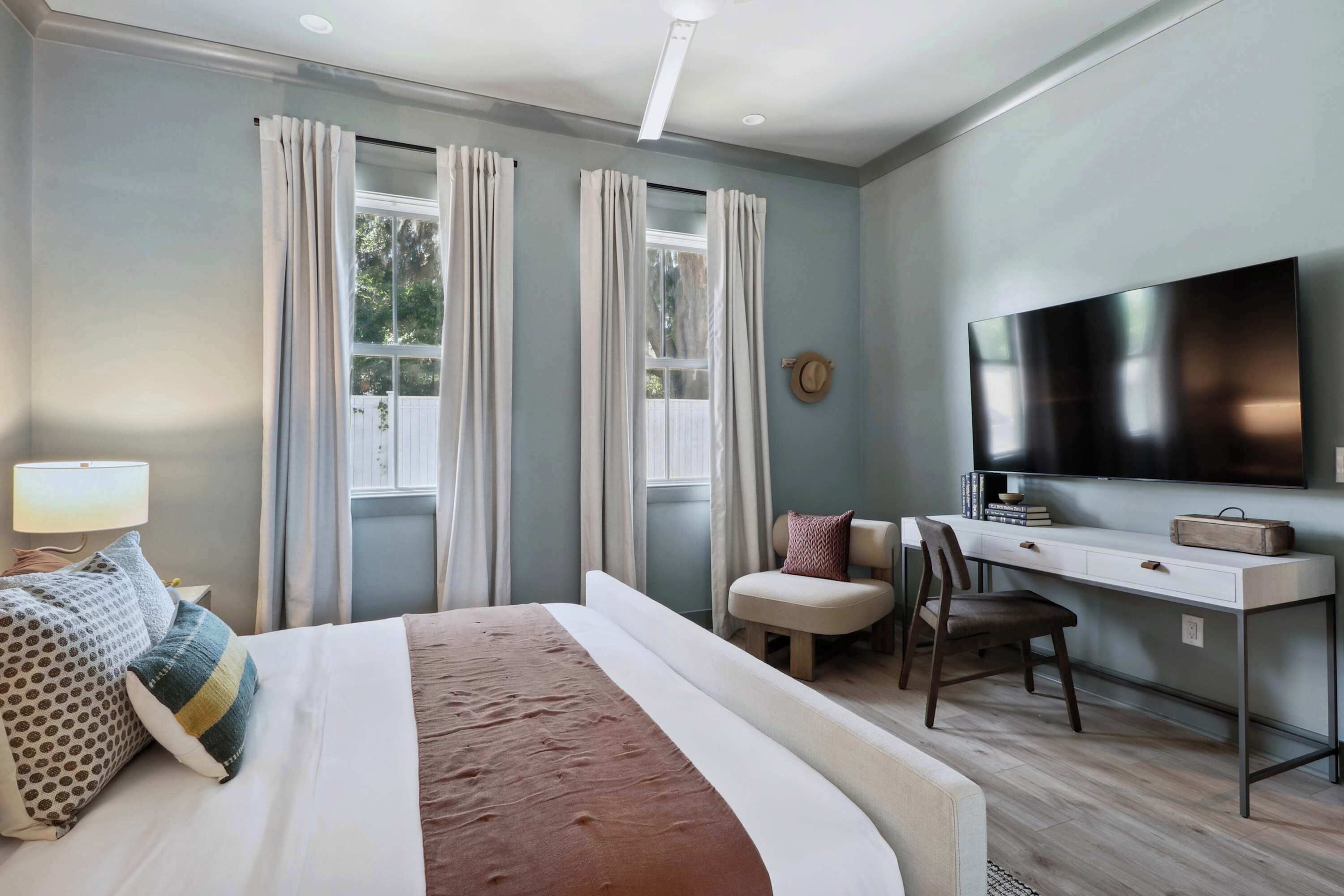 Una habitación de hotel moderna con una cama grande, un escritorio con silla, un televisor de pantalla plana y una ventana con cortinas.