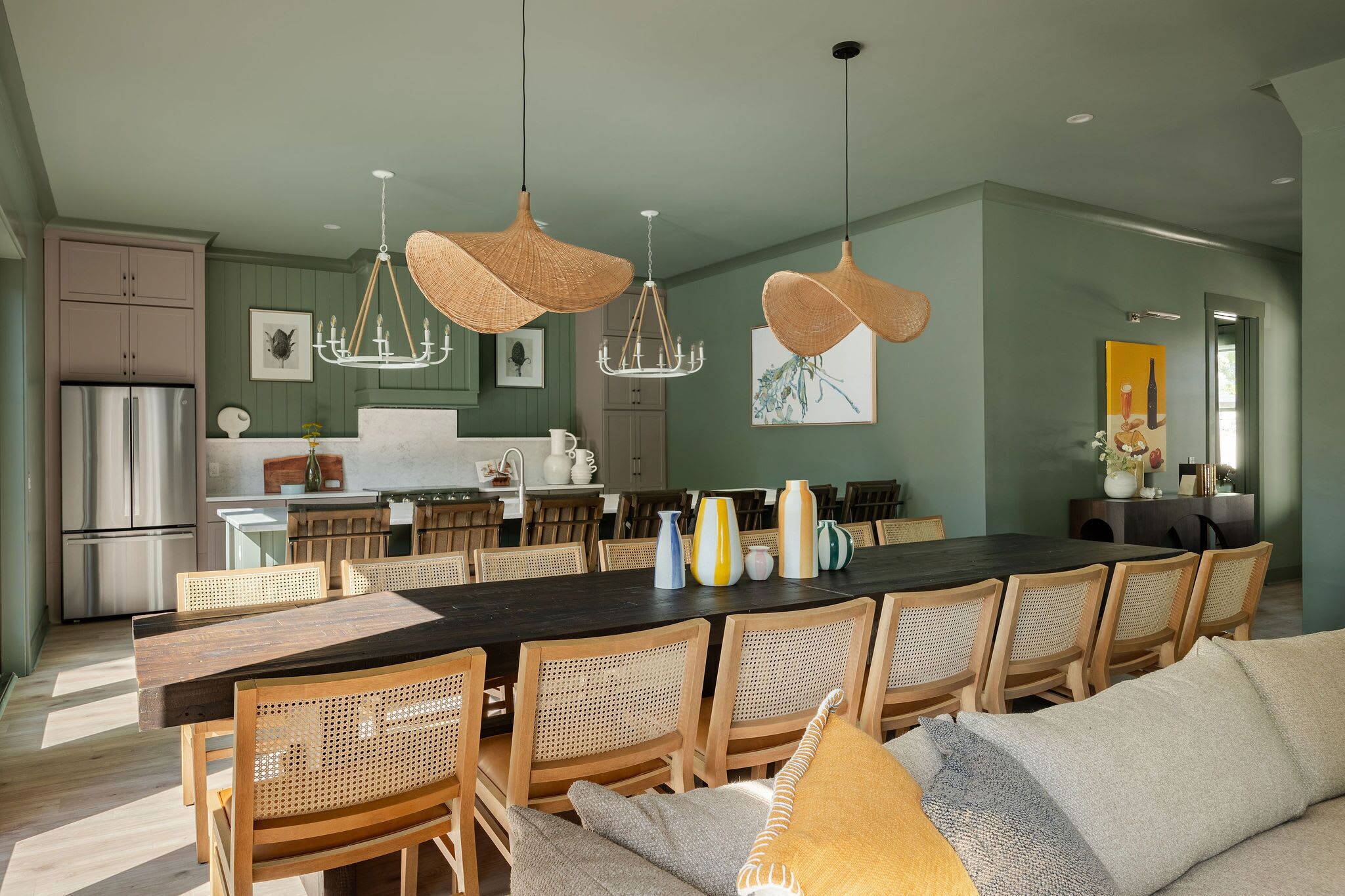 A spacious kitchen with a dining area, featuring a long wooden table, wicker chairs, and hanging wicker chandeliers.