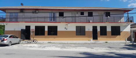 A two-story building with a flat roof, a balcony on the upper floor, and a ground floor entrance.