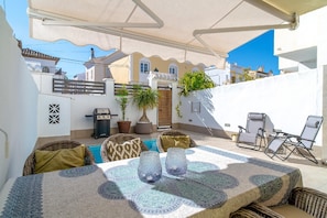 Relax in the covered patio area with a dining table, barbecue grill, and pool, surrounded by wicker chairs and a pergola.