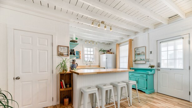 Une cuisine avec un plancher en bois, des meubles de couleur blanche, un mur d’accent turquoise et un coin bar avec des tabourets.