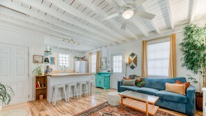 Un vaste espace de vie avec un canapé bleu, un plancher en bois et un coin cuisine doté de meubles blancs et d’un îlot de couleur turquoise.