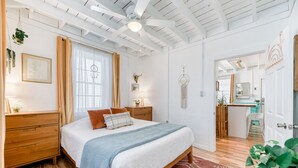 Une chambre avec un grand lit, des tables de chevet en bois, un tapis rouge à motifs et un ventilateur de plafond.